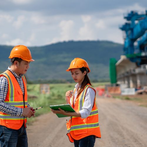 Survey team is working with a theodolite and road construction plans. Civil engineers are taking measurements with surveying tools during the construction.
